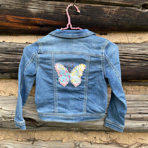 Blue denim jacket with a butterfly design on a wooden background