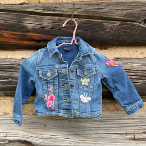 Children's denim jacket with floral and butterfly patches on a wooden background