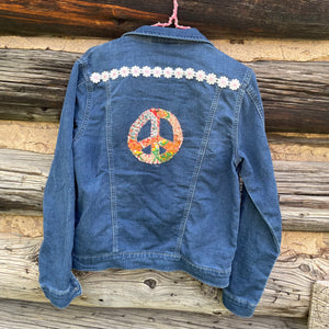 Blue denim jacket with floral peace symbol and white flowers on a wooden background