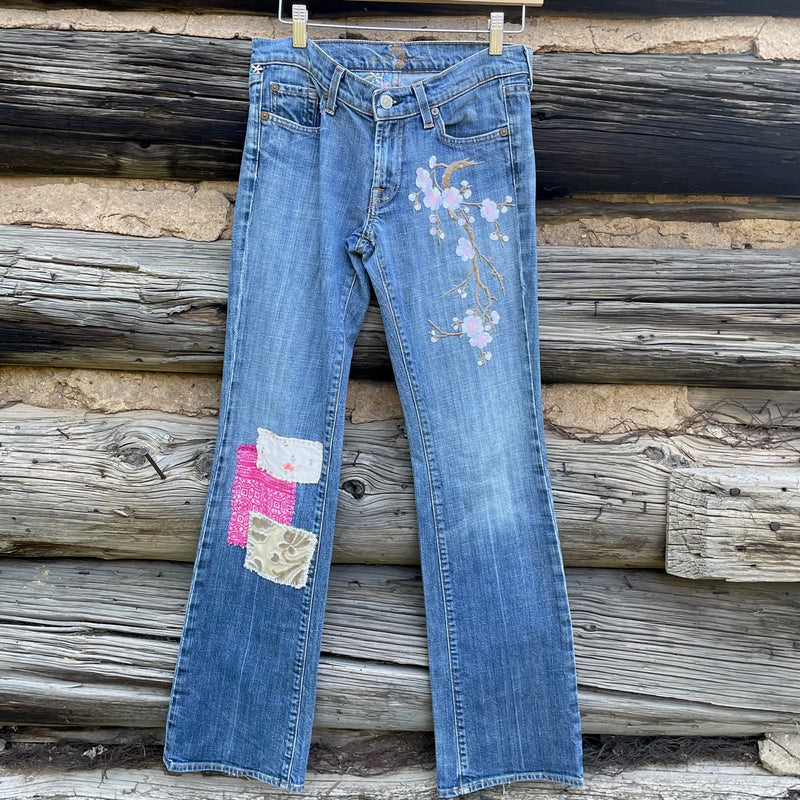 Front of jeans with patches sewn on left leg and a flower patch on the right leg.