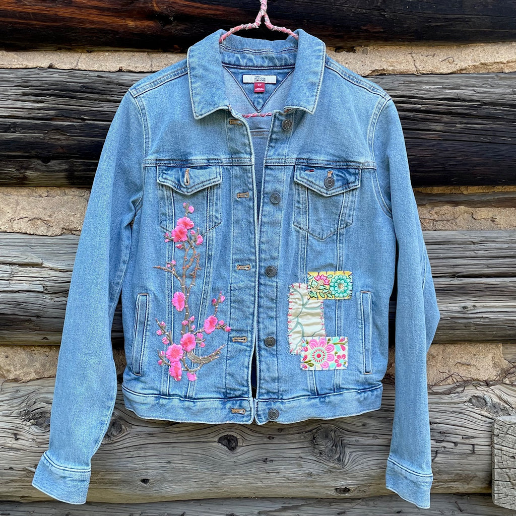 Front of Jean jacket with flower patch on left side and three sewn fabric patches on the right side.