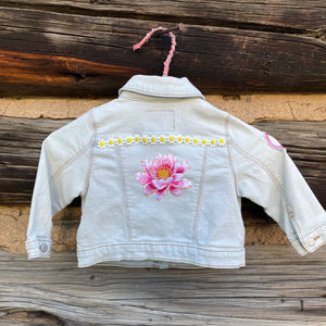 Back of light wash denim jacket with flower patch.