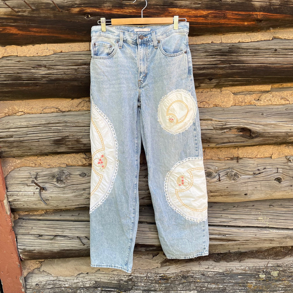 Light blue jeans with floral patches hanging against a wooden wall.