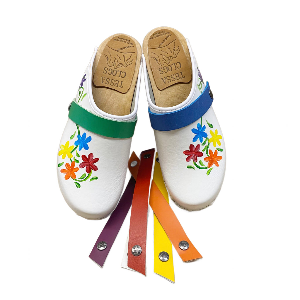 Traditional heel with handpainted Axelina design in pride colors of red, orange, yellow, blue, and purple flowers. The grass green snap strap is shown on the left clog and the blue is displayed on the right.