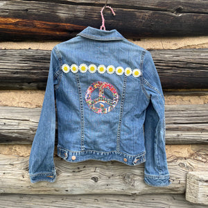 Denim jacket with peace symbol and flower designs on a wooden background