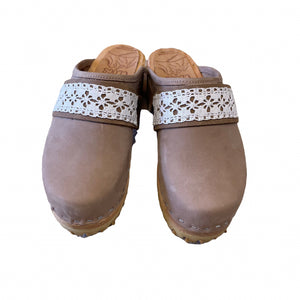 A pair of taupe leather clogs with white floral lace straps, shown from a top-down view on a white background.