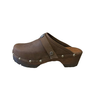 A pair of brown leather clogs with pewter metal studs and a decorative pewter buffalo medallion on the strap, shown on a plain white background.