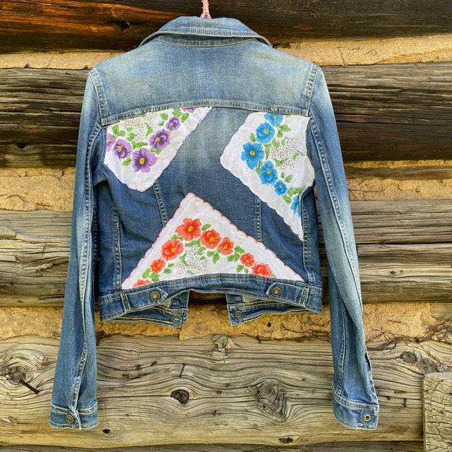 Back of jean jacket with three vintage napkin patches in triangular shapes sewn on.