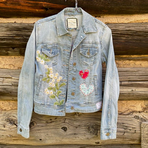 Front of jean jacket with large flower patch on left and two fabric heart patches on the right.