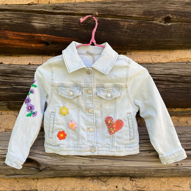 Front of jean jacket with flower and heart patches sewn on.