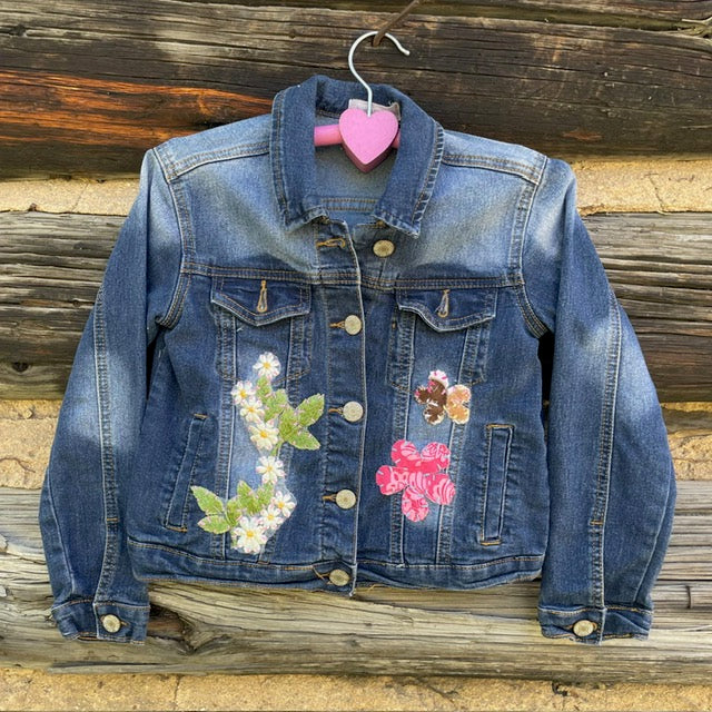 Front of jean jacket with white flower on left and two fabric flower patches on the right.