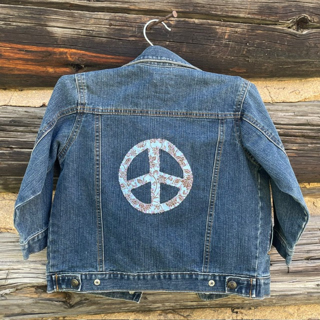 Back of jean jacket with large light blue peace sign patch.