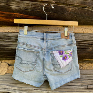 Back of jean shorts with purple flowered napkin sewn on right pocket.