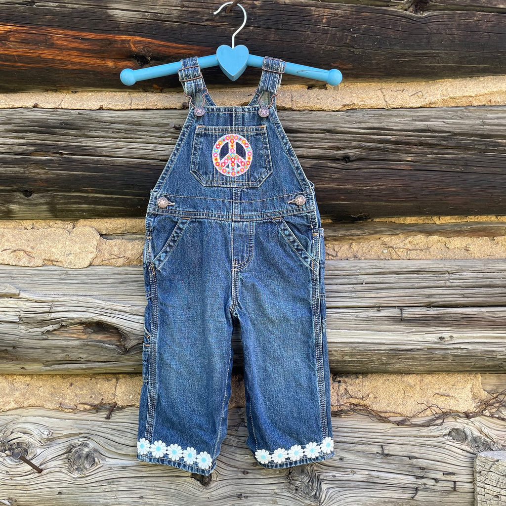 Front of jean overalls with peace sign patch and daisy chain cuff.