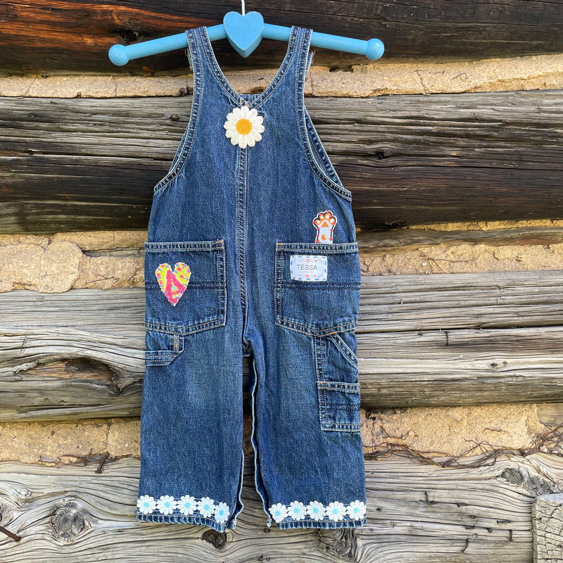 Back of jean overalls with daisy patch, heart patch, cat paw patch, and daisy chain cuff.