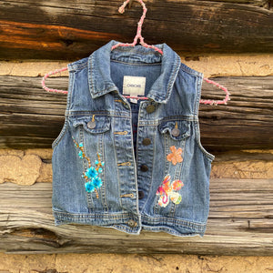 Denim vest with floral embroidery on a wooden background