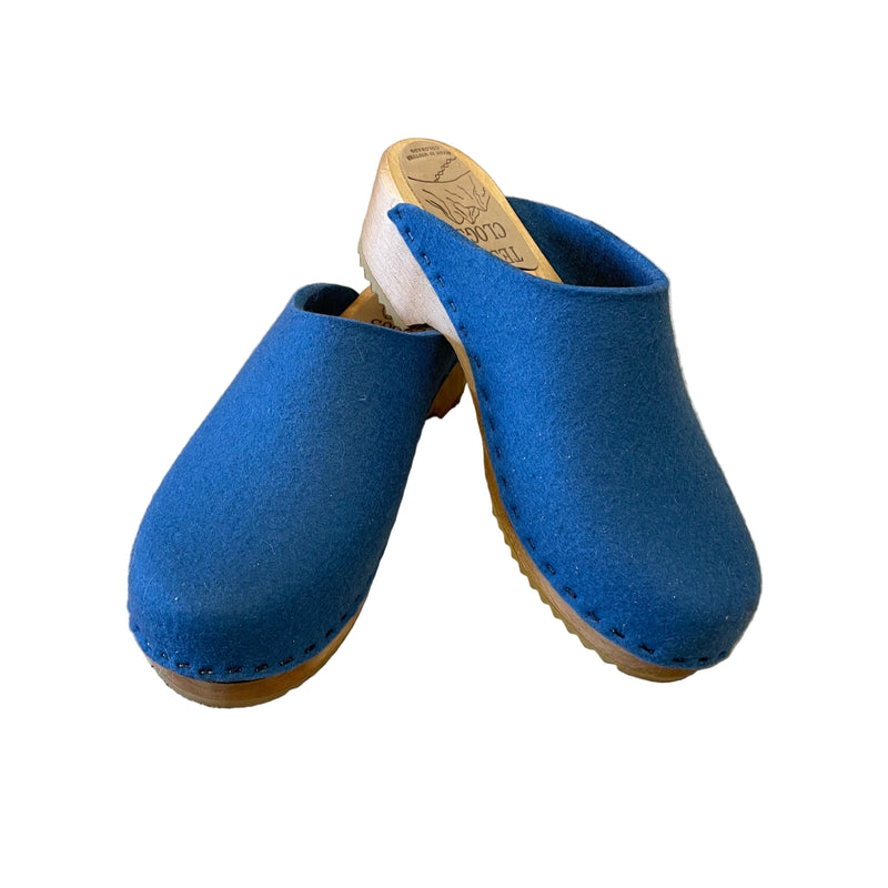 Pair of blue clogs with brown soles on a beige surface