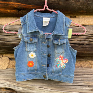 Blue denim vest with floral patches on a wooden surface