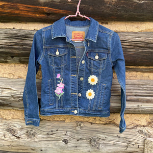 Blue denim jacket with floral patches on a wooden background