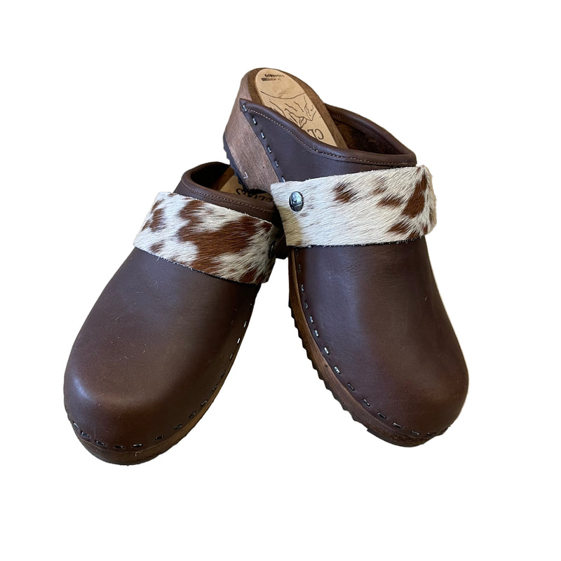 Pair of brown clogs with cowhide straps on a white surface