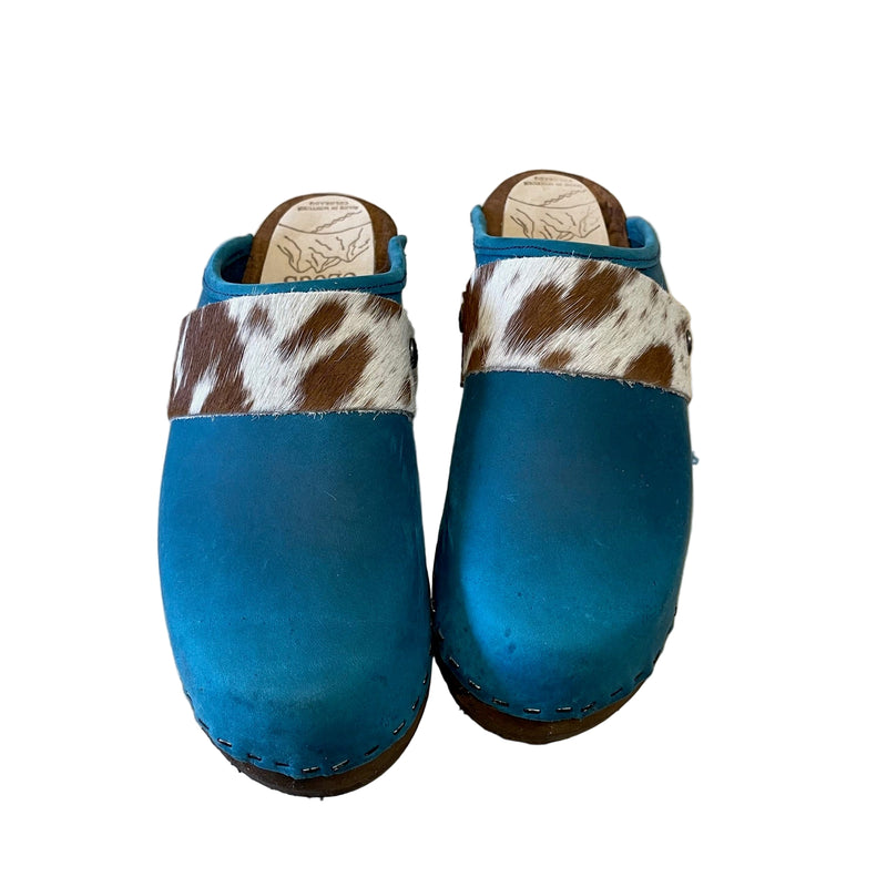 Blue clogs with cow print straps on a white surface