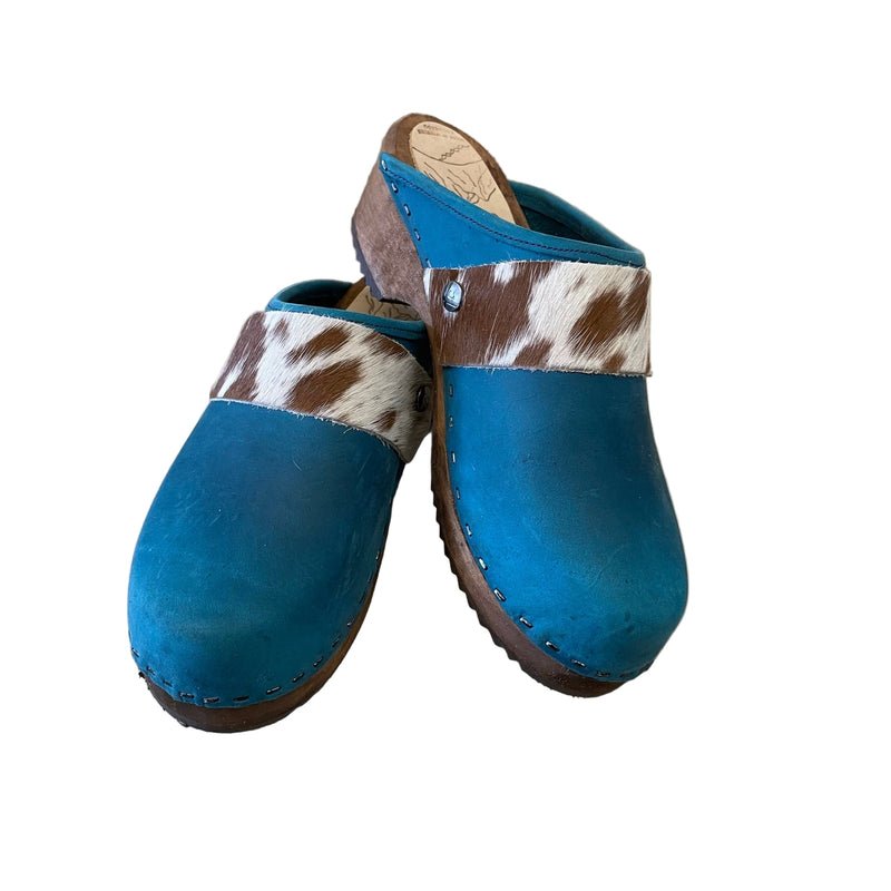 Pair of blue clogs with cowhide straps on a white surface