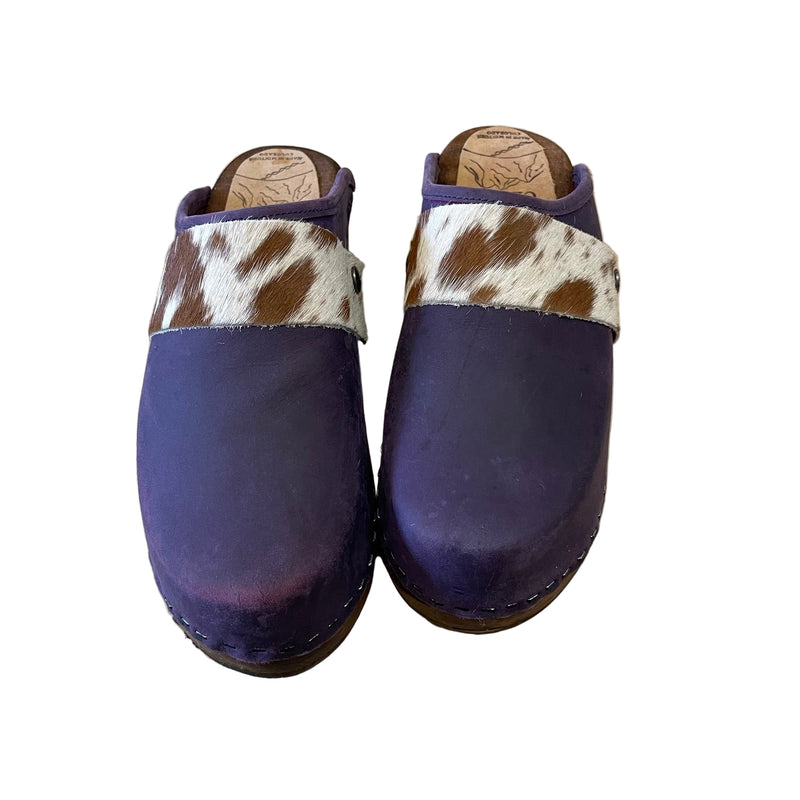 Pair of purple clogs with cowhide pattern straps on a white surface
