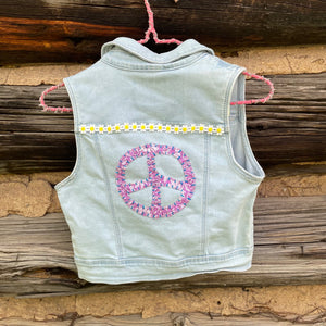 Light blue denim vest with pink peace symbol on a wooden background