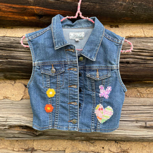 Denim vest with floral and butterfly patches on a wooden background