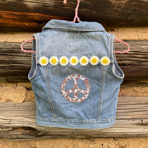 Denim vest with peace symbol and flowers hanging against a wooden background