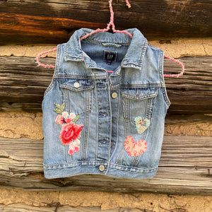 Denim vest with floral embroidery on a wooden background